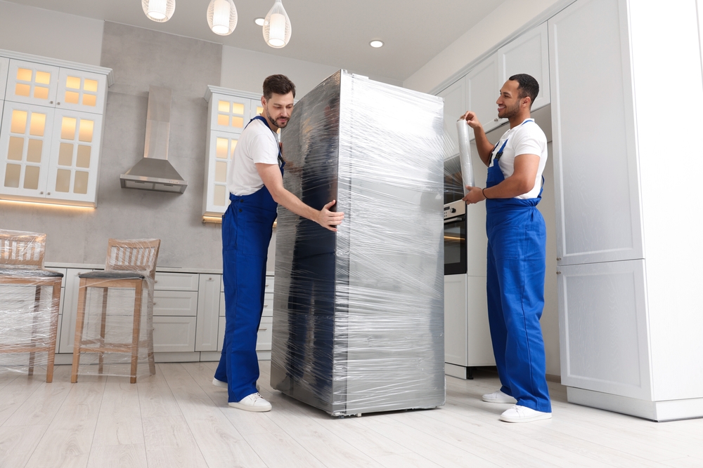 Movers using protective pads and a dolly to move a refrigerator without damaging hardwood floors